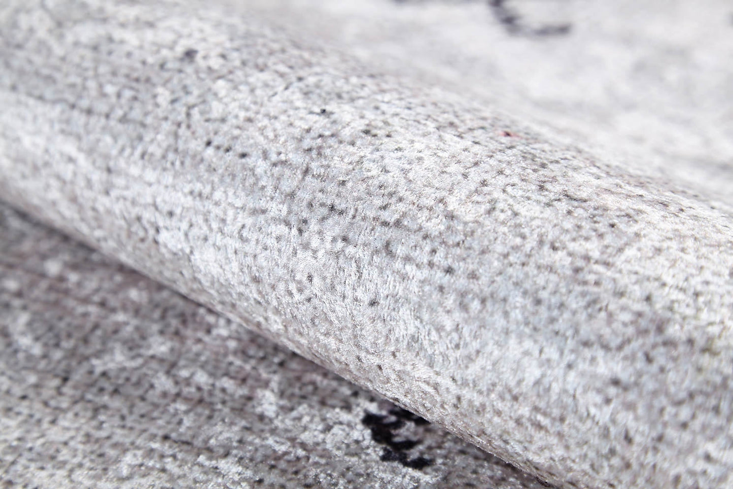 Close-up of the Tribal Tassel - Washable Rug - JR1683 (Custom Size) in light grey, featuring a soft, dense fiber surface with subtle speckles and shading. Allergy-sensitive material resembles plush cream and beige rugs, shown partially rolled.