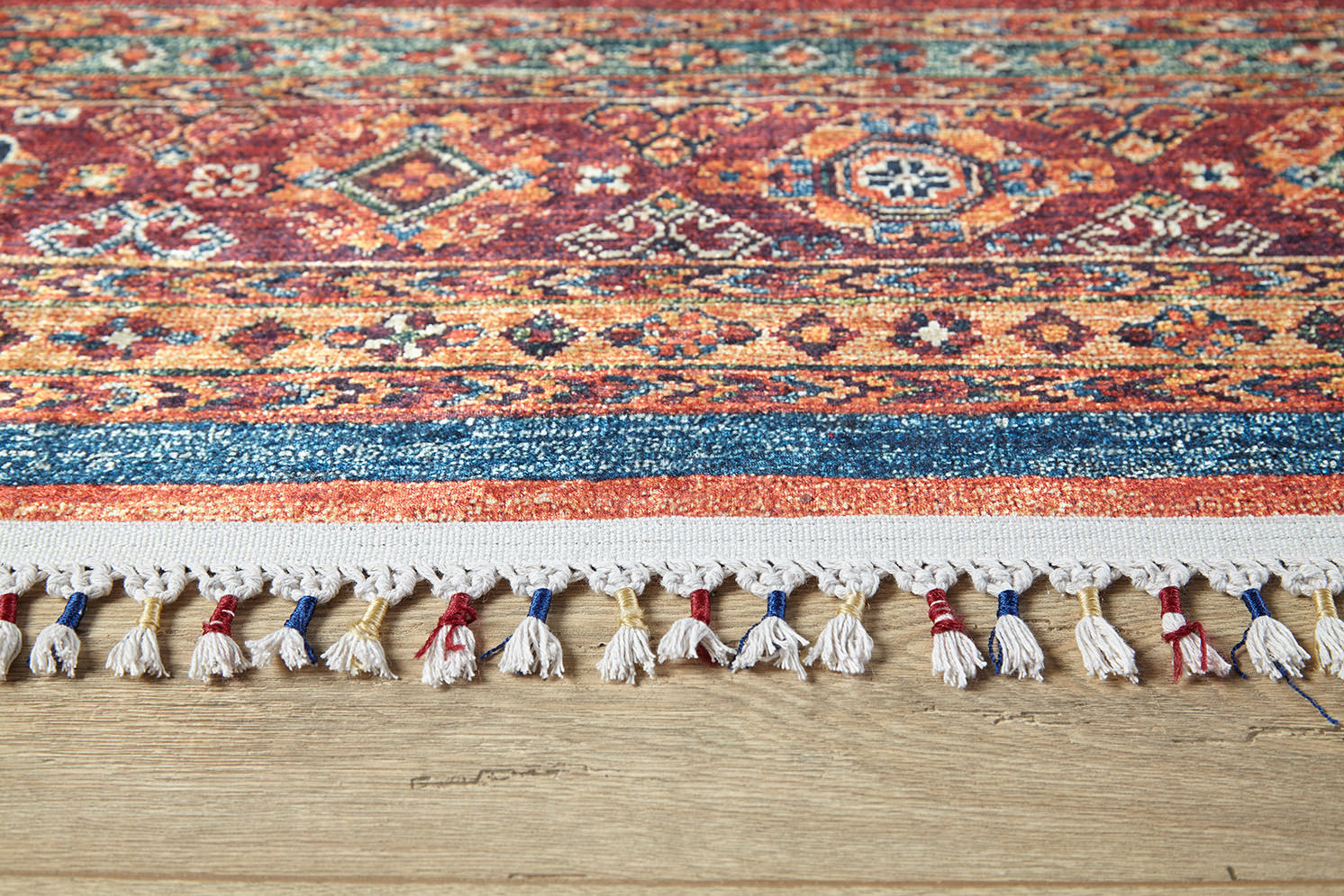 A close-up of the Tropic Thunder - Washable Rug - JR5077 (Custom Size) shows its allergy-friendly, vibrant multicolor geometric design with tassels, placed on a light wooden floor—perfect for adding style to any space.