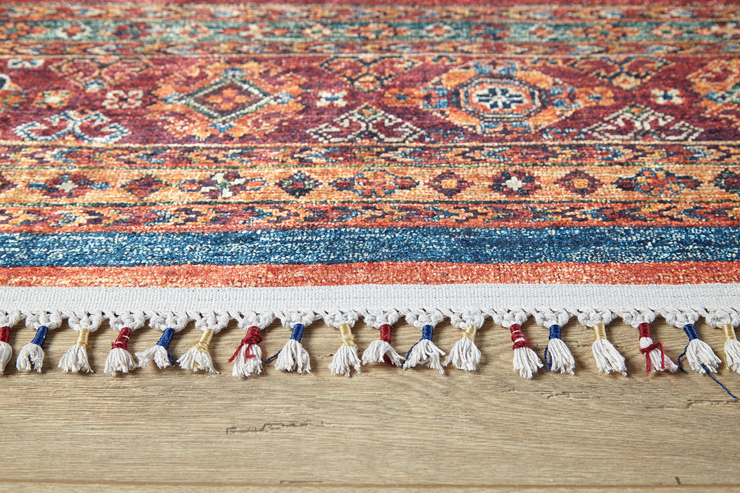 A close-up of the Tropic Thunder - Washable Rug - JR5077 (Custom Size) shows its allergy-friendly, vibrant multicolor geometric design with tassels, placed on a light wooden floor—perfect for adding style to any space.