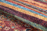 A close-up of the Tropic Thunder - Washable Rug - JR5077 (Custom Size) reveals multicolor horizontal stripes in red, yellow, and blue with detailed floral and geometric patterns in the background.