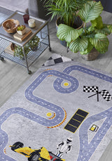 The Turbo Tracks - Machine-Washable Rug JRC089 (Custom Size) with a racetrack, finish line, and race car design is displayed on a light wood floor beside a metal cart with wooden bowls and potted plants, plus large leafy plants in the background.