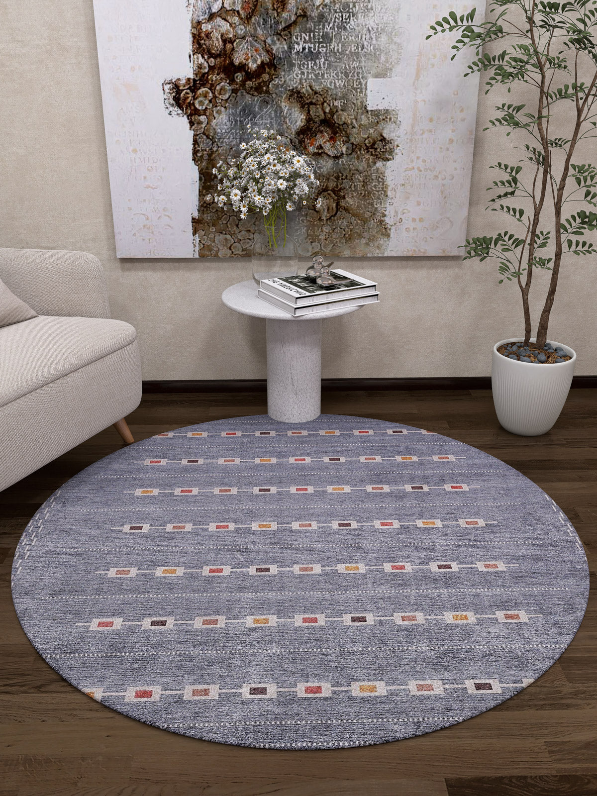A cozy modern living room featuring the Tuscan Villa - Washable Rug - JR5058 (Custom Size) in round gray-anthracite, paired with a small white sofa, circular side table with books and flowers, tall potted plant, and abstract wall art—ideal for busy spaces.