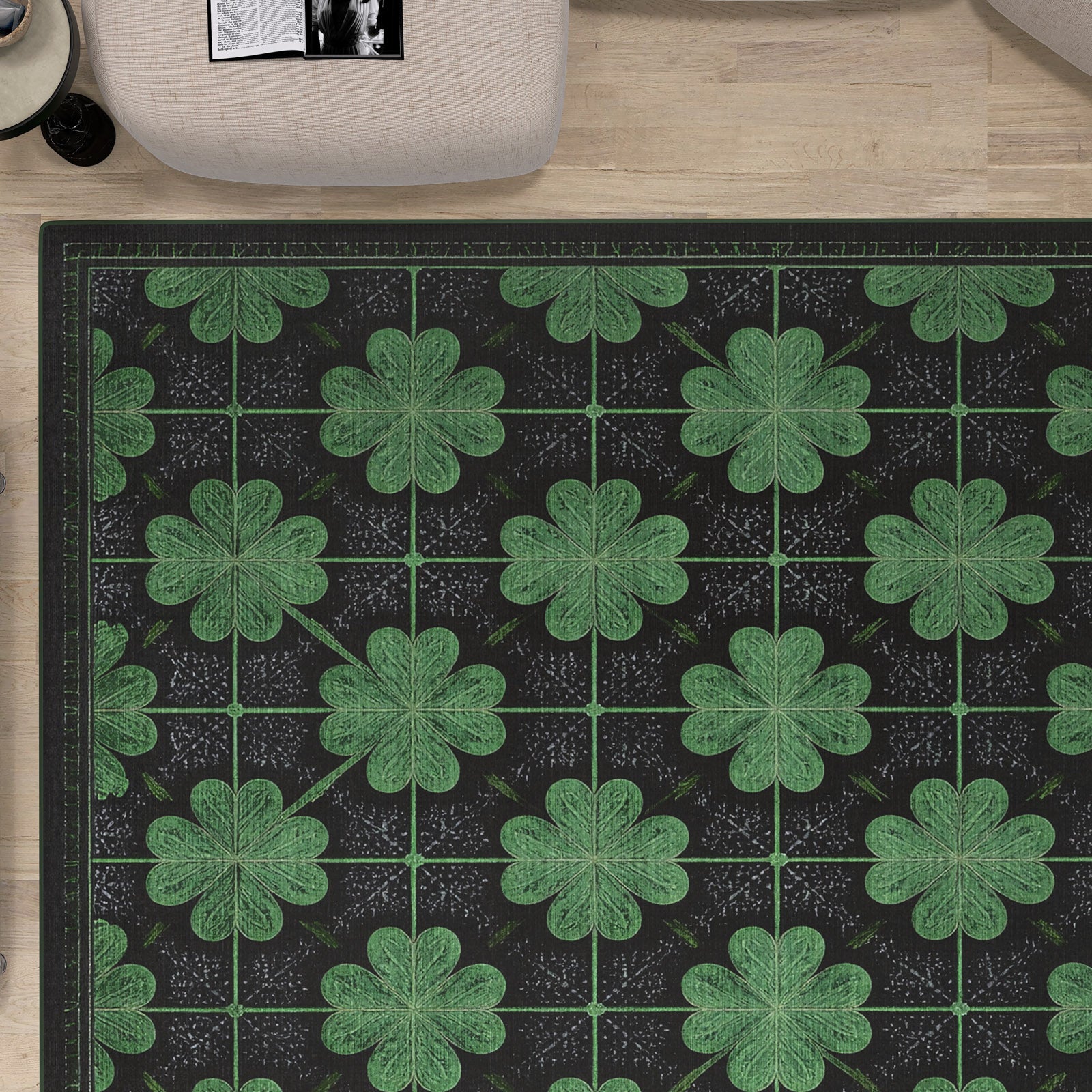 A top-down view of the Clover Noir - Washable Rug - JRS012, featuring a repeating green four-leaf clover pattern on a dark background, perfect for high-traffic areas, placed on light wood flooring near light chairs and an open magazine.
