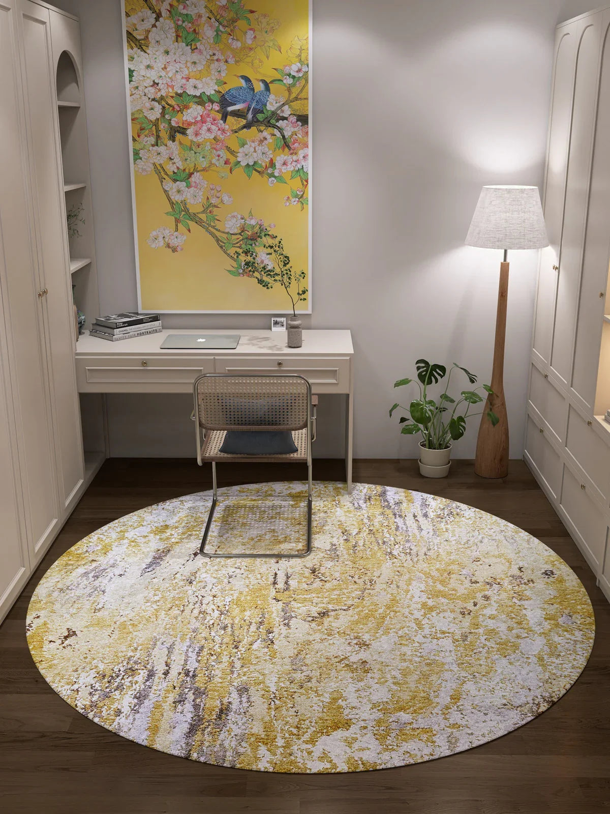 A tidy home office with a white desk, chair, lamp, tall plant, and floral bird artwork above the desk. The floor features the Color Splash - Washable Rug - JR146 in yellow-gold with white patterns—ideal for high-traffic areas.