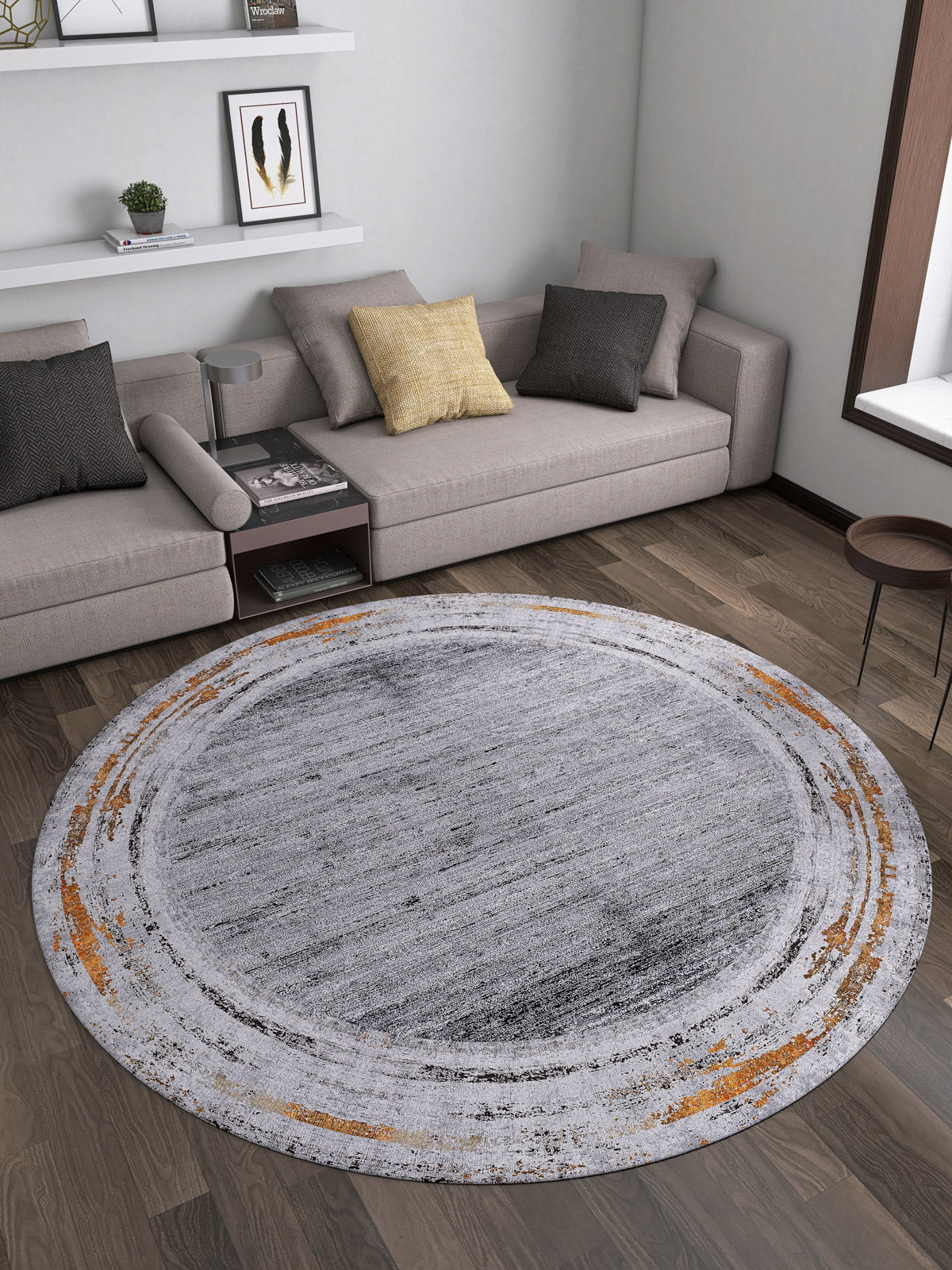 A modern living room with gray sectional sofas, a yellow cushion, wall shelves with decor, and the Bold and Chic - Washable Rug - JR1198 (Outlet) US featuring a distressed gray and orange circular pattern on the wooden floor.