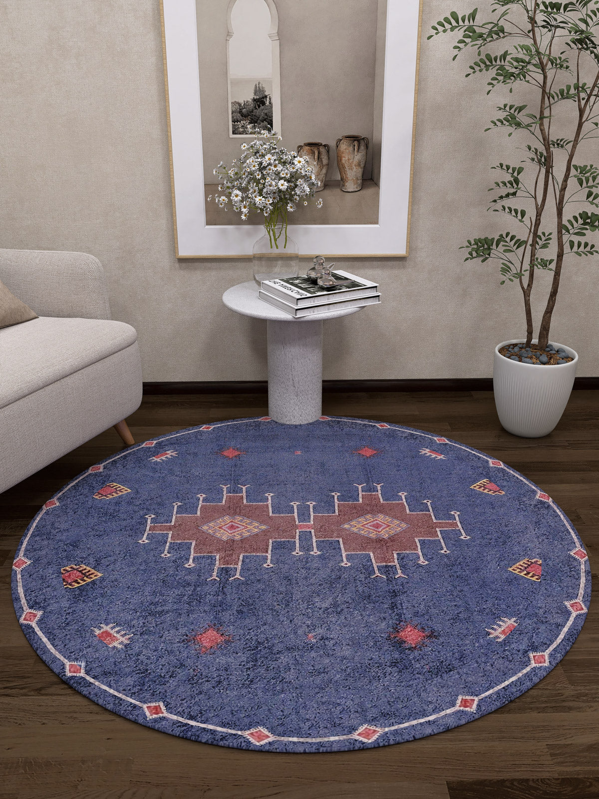 A living room corner features the Boho Chic Tapestry - Washable Rug - JR5083 with red and white geometric patterns, a light sofa, round side table with flowers and books, a potted plant, and framed wall art above the table.