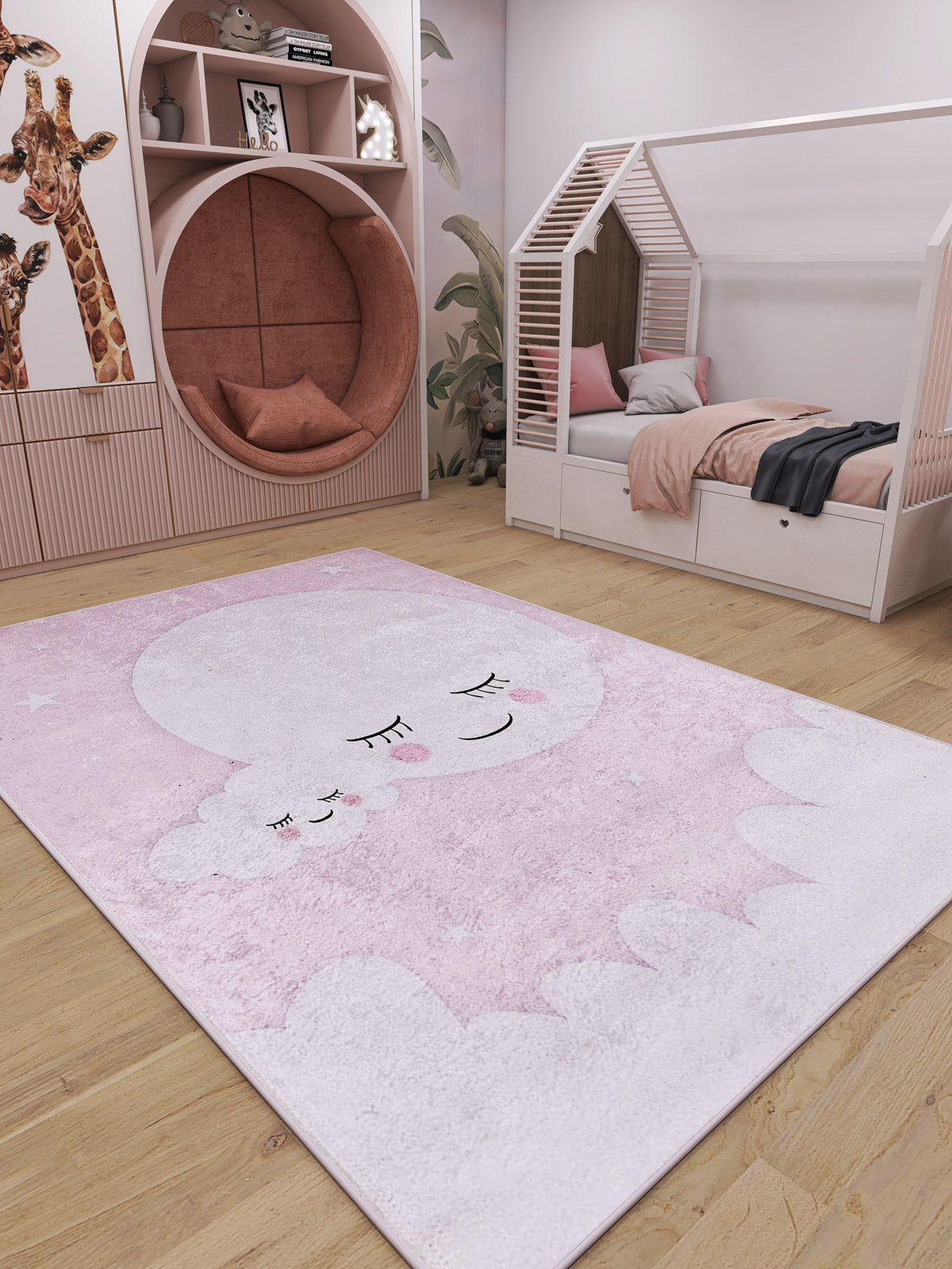A cozy kids’ room with pink and white decor features a round reading nook, house-shaped bed, giraffe wall art, and the Cosmic Naptime - Machine-Washable Rug JRC032 in soft pink with a sleeping moon and cloud design.