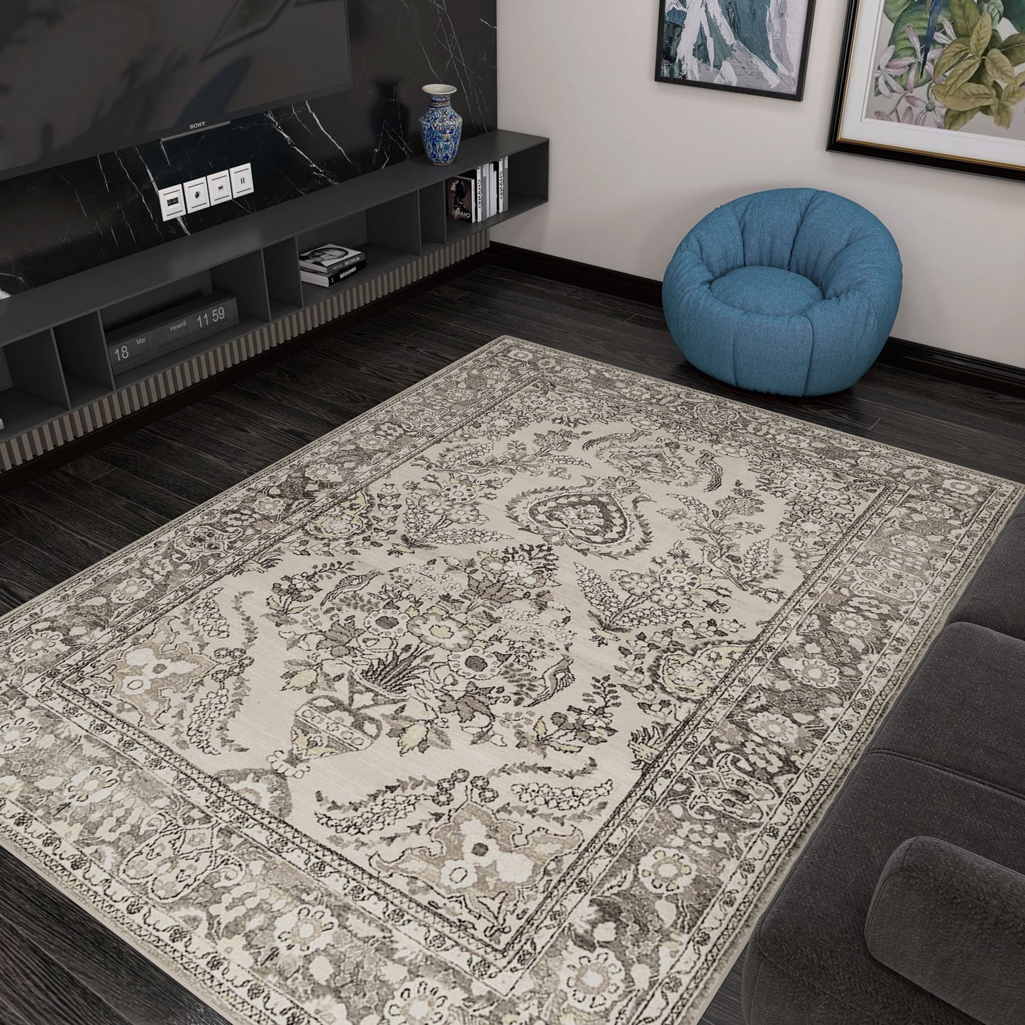 The Velvet Mosaic - Washable Rug (JRN1004), featuring a beige and brown floral Oriental border, is placed on a dark wood floor in a modern living room beside a gray sofa, blue bean bag, and black entertainment unit with TV and decor.