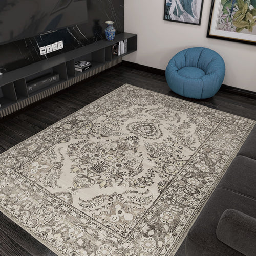Load image 1 in gallery view. The Velvet Mosaic - Washable Rug (JRN1004), featuring a beige and brown floral Oriental border, is placed on a dark wood floor in a modern living room beside a gray sofa, blue bean bag, and black entertainment unit with TV and decor.