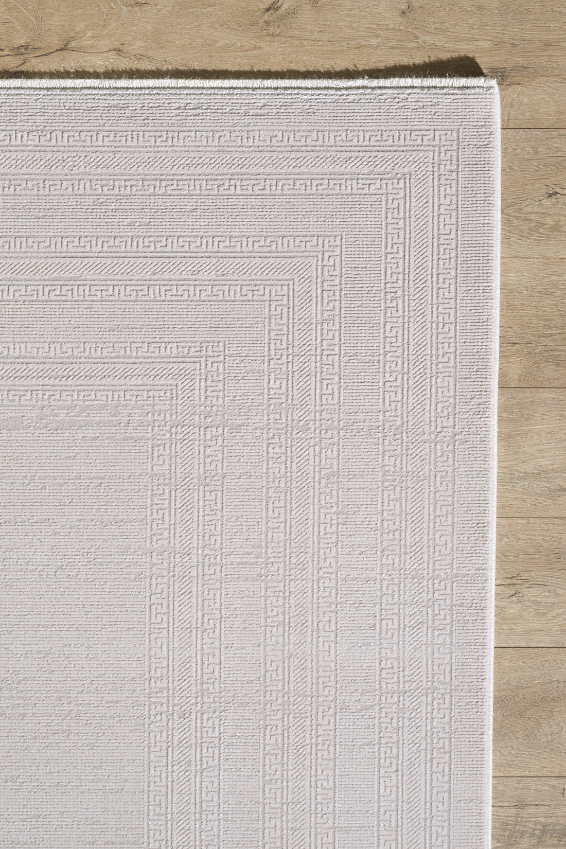 The Vanilla Dream Modern Bordered Rug - EW2742 features a light beige hue and subtle geometric border, displayed on a light wooden floor. Only part of this machine-made rug is shown, highlighting clean edges and its soft, textured design.