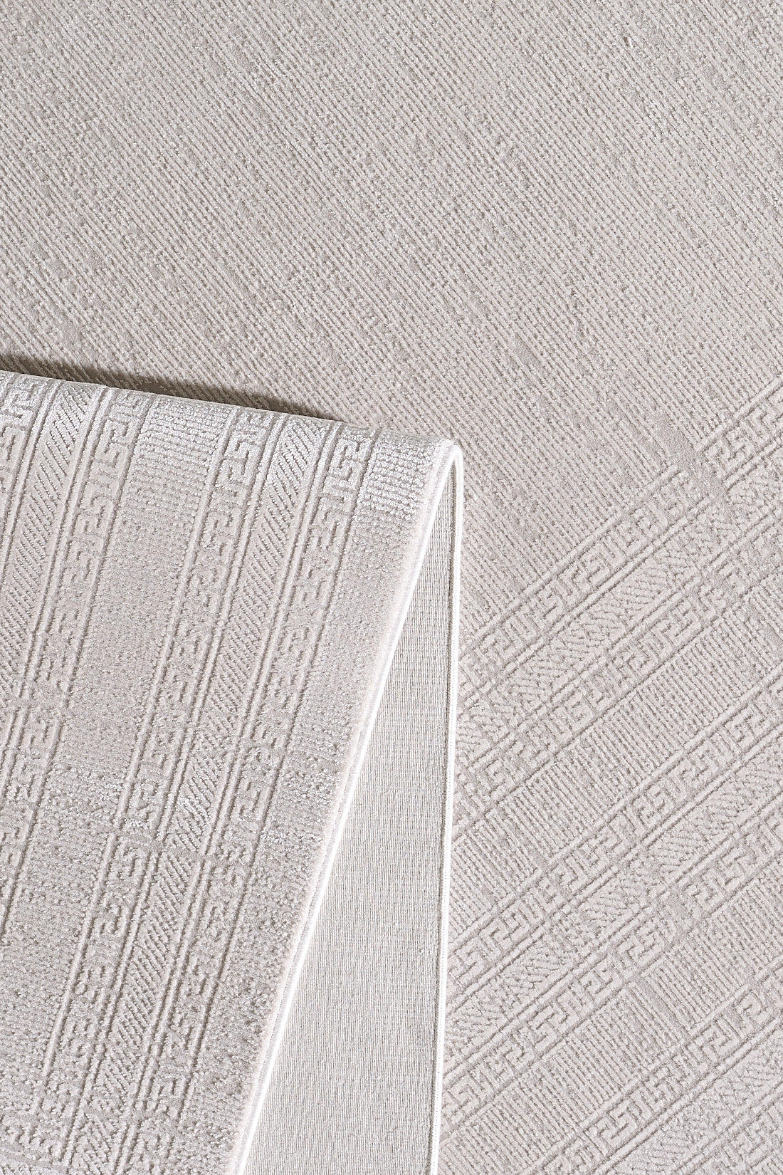 The Vanilla Dream Modern Bordered Rug - EW2742, in folded beige, displays subtle geometric and Greek key motifs atop a matching textured fabric, highlighting its intricate woven details and soft, neutral tones.