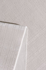 The Vanilla Dream Modern Bordered Rug - EW2742, in folded beige, displays subtle geometric and Greek key motifs atop a matching textured fabric, highlighting its intricate woven details and soft, neutral tones.