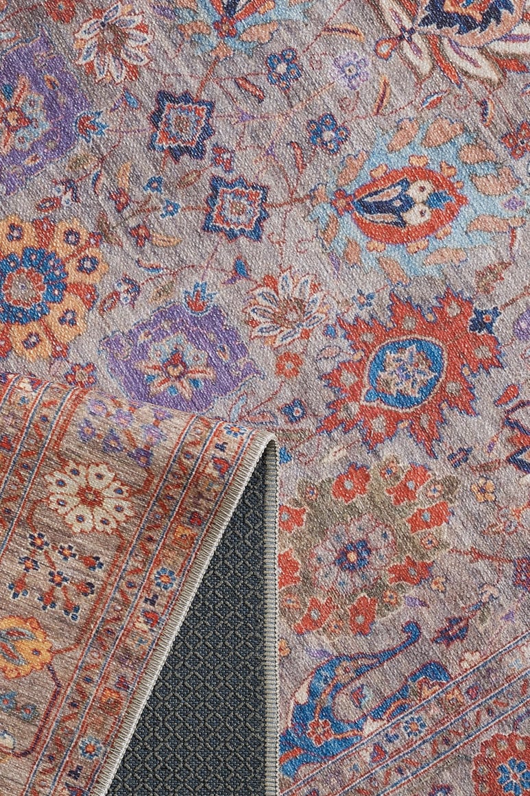 The Velorio Floral Washable Rug - LCC3006 features intricate floral and geometric patterns in red, blue, orange, and purple. A folded corner reveals its textured dark backing, making it ideal for high-traffic areas.