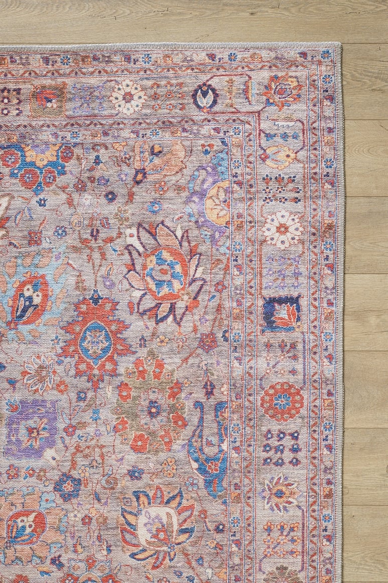 A close-up of the Velorio Floral Washable Rug - LCC3006, featuring intricate red, blue, orange, and beige floral and geometric patterns on a light wood floor—perfect for allergy-sensitive homes or high-traffic areas.