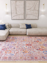 A modern living room with a light beige sectional, two blue accent pillows, abstract wall art, wall sconces, and the Velorio Floral Washable Rug - LCC3006 (Custom Size)—ideal for high-traffic areas—on a light wood floor.