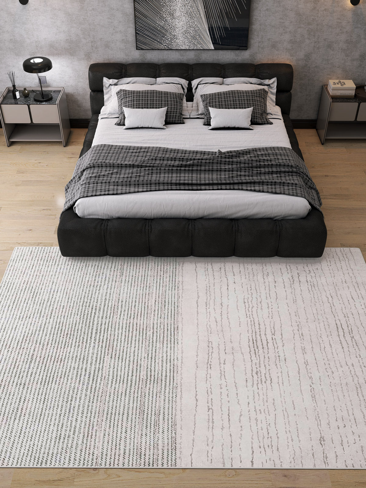 A modern bedroom features a large bed with gray and white bedding, two bedside tables with lamps, and the Velvet Echo - Washable Rug - JRN25 on the wood floor—perfect for busy spaces. Monochrome abstract artwork adorns the wall behind the bed.