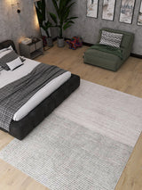 A modern bedroom with a low black bed, gray bedding, green lounge chair, large plant, wall art, and the Velvet Echo - Washable Rug - JRN25 (Custom Size), perfect for high-traffic wooden floors. A colorful elephant decor piece is by the chair.