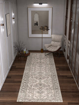 A modern hallway with wooden floors features the Velvet Mosaic - Washable Rug - JRN1004 in a patterned cream design, complemented by an armchair with a cushion, a floor lamp, framed artwork, and bookshelves for stylish convenience.