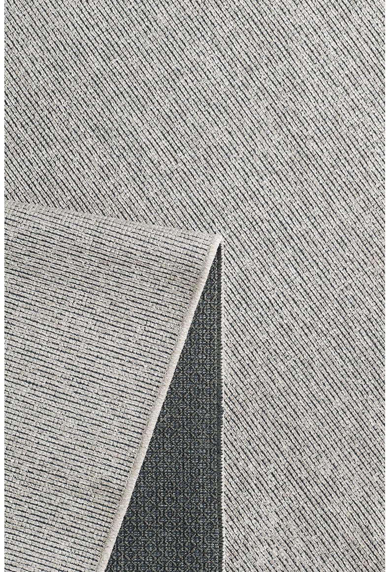 The Velvet Touch Cream Area Rug - PST001 is displayed with a flipped corner, revealing its darker patterned underside. The rug showcases a subtle linear design on the front, adding a fresh, modern look to any space.