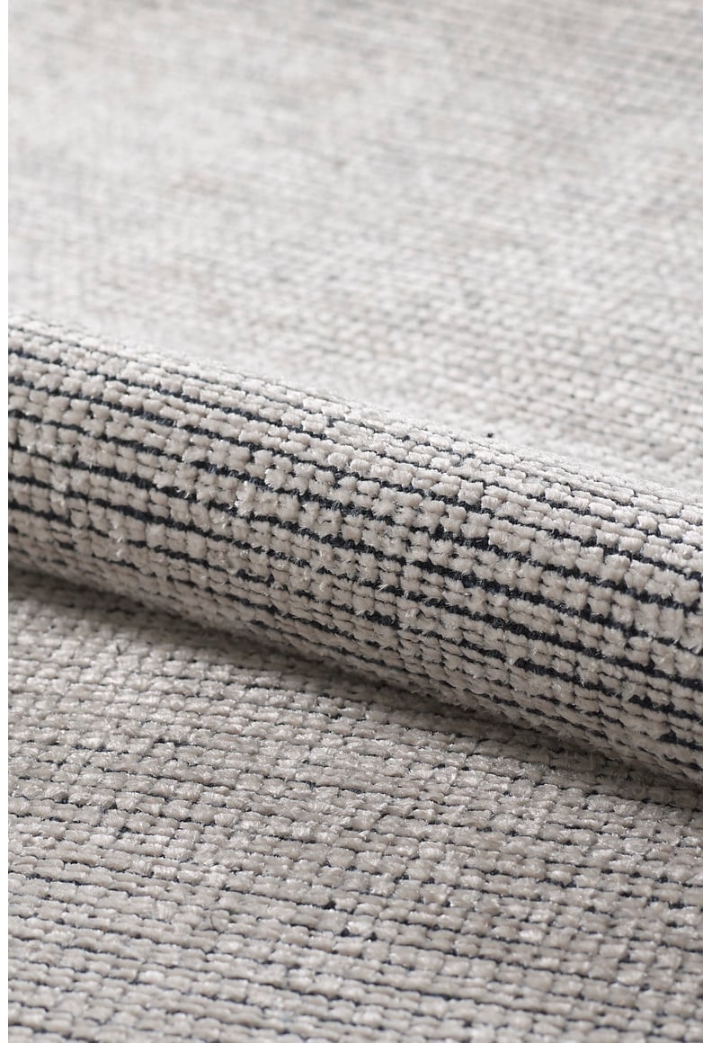 Close-up of the Velvet Touch Cream Area Rug - PST001, featuring a light gray hue with a subtle black linear pattern, partially rolled to reveal its textured surface and plush, thick weave for a modern style accent.