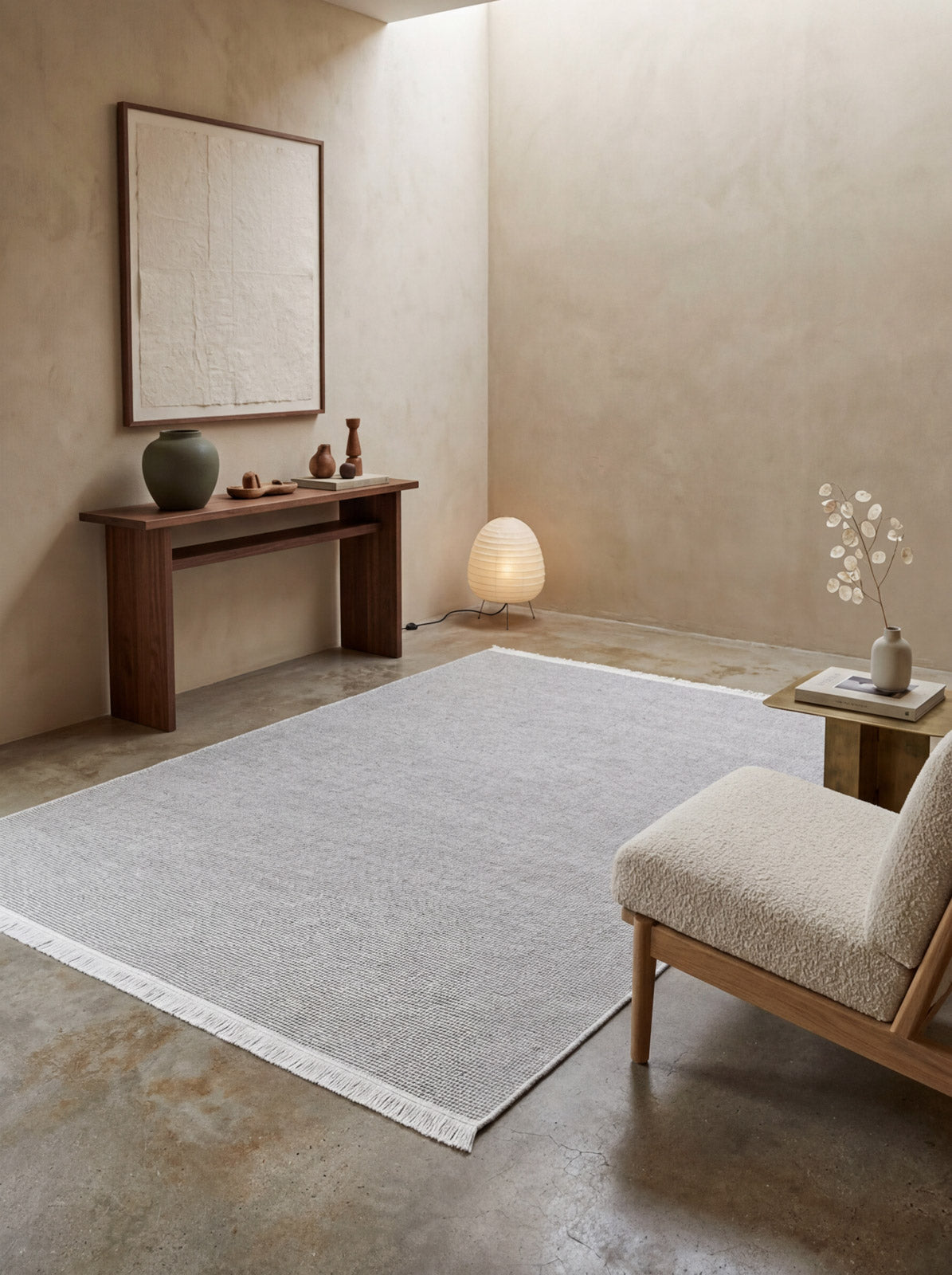Minimalist living room featuring the Velvet Touch Cream Area Rug - PST001, a wooden console table with ceramics, a glowing floor lamp, and a modern chair with a textured cream cushion against beige walls and concrete flooring.