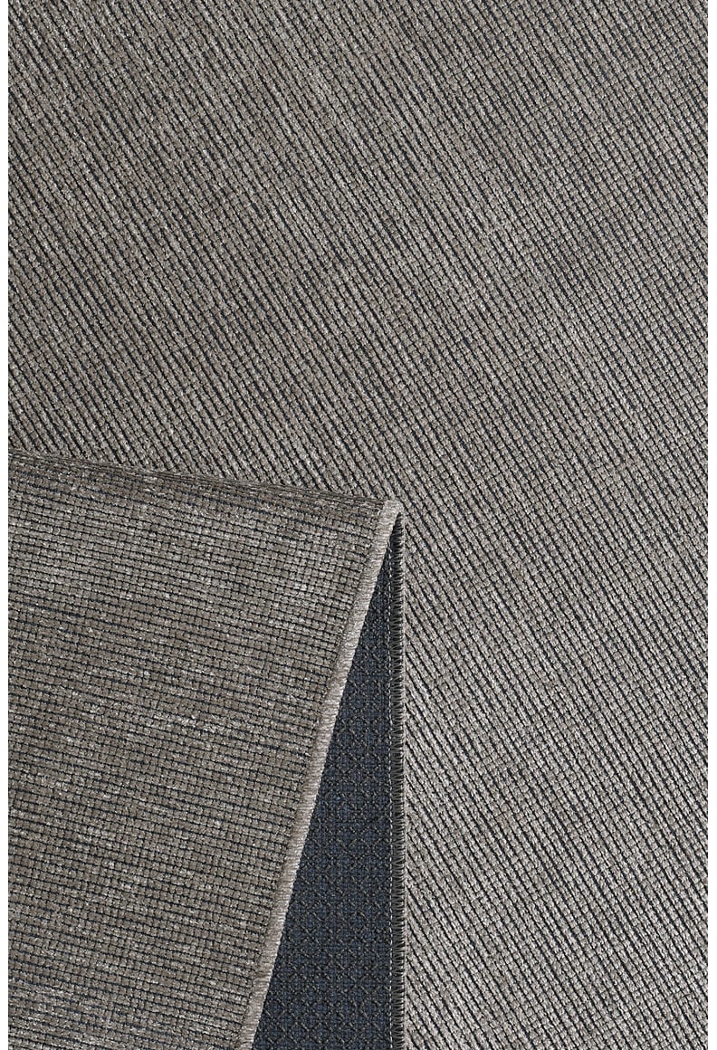 A close-up of the Velvet Touch Gray Area Rug - PST003 shows its textured diagonal pattern and a folded corner revealing the dark non-slip backing—ideal for adding minimalist style to your space.