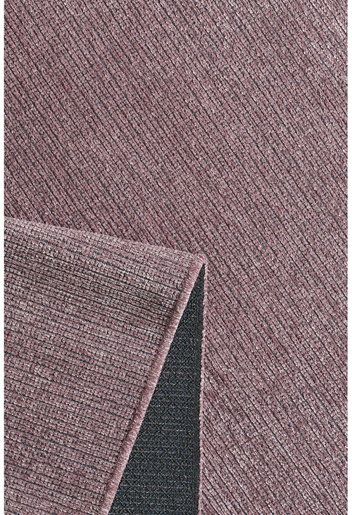 Load image 1 in gallery view. A close-up of the Velvet Touch Pink Area Rug - PST005 shows its textured mauve surface with diagonal lines. A lifted corner reveals the contrasting dark gray, non-slip backing—ideal for adding modern style to any room.