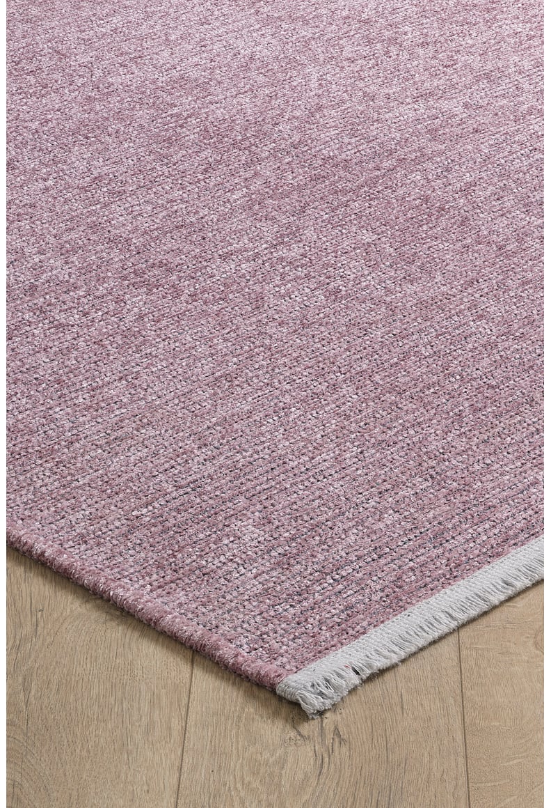 A close-up of the Velvet Touch Pink Area Rug - PST004 shows its woven textured surface and short light gray fringe, styled in a contemporary look and placed on a light wood floor.