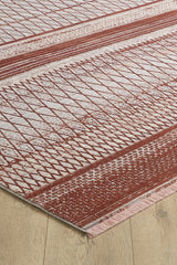 A close-up of the Vibrant Bohemian Trellis Rug - HRD009, a machine-made viscose-polyester rug with rust red and off-white geometric patterns, including diamonds and stripes, and fringed edges on a light wood floor.