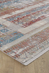 A close-up of the Vibrant Nomadica Premium Rug - M366C showcases red, blue, cream, and gold traditional motifs on a wooden floor. This machine-made rug features fringed edges and an intricately detailed, slightly distressed look.