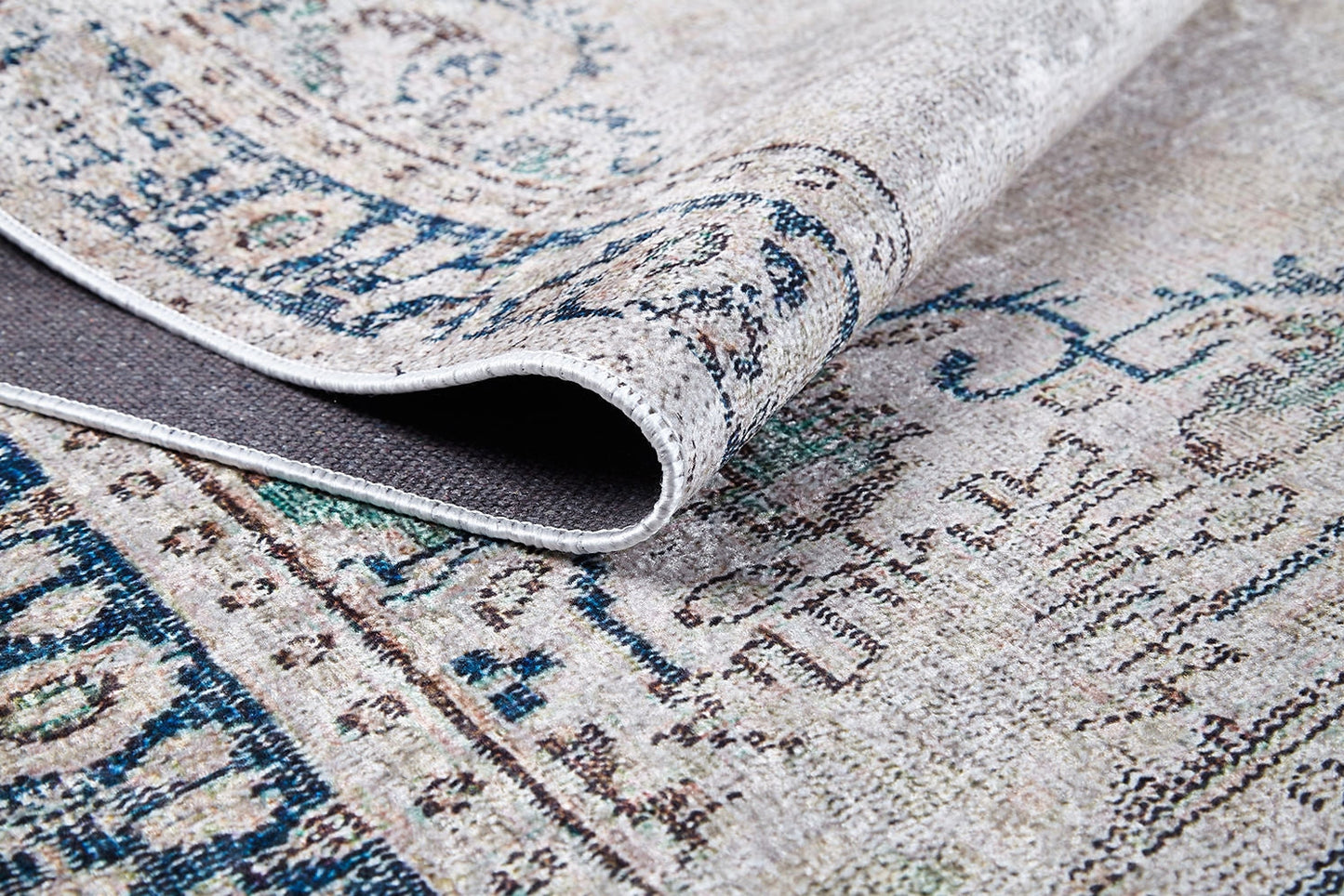 A close-up of the Vintage Beauty - Washable Rug - JR1688 (Custom Size) showcases its intricate blue and beige designs, with a folded corner revealing the underside and texture—ideal for high-traffic areas.
