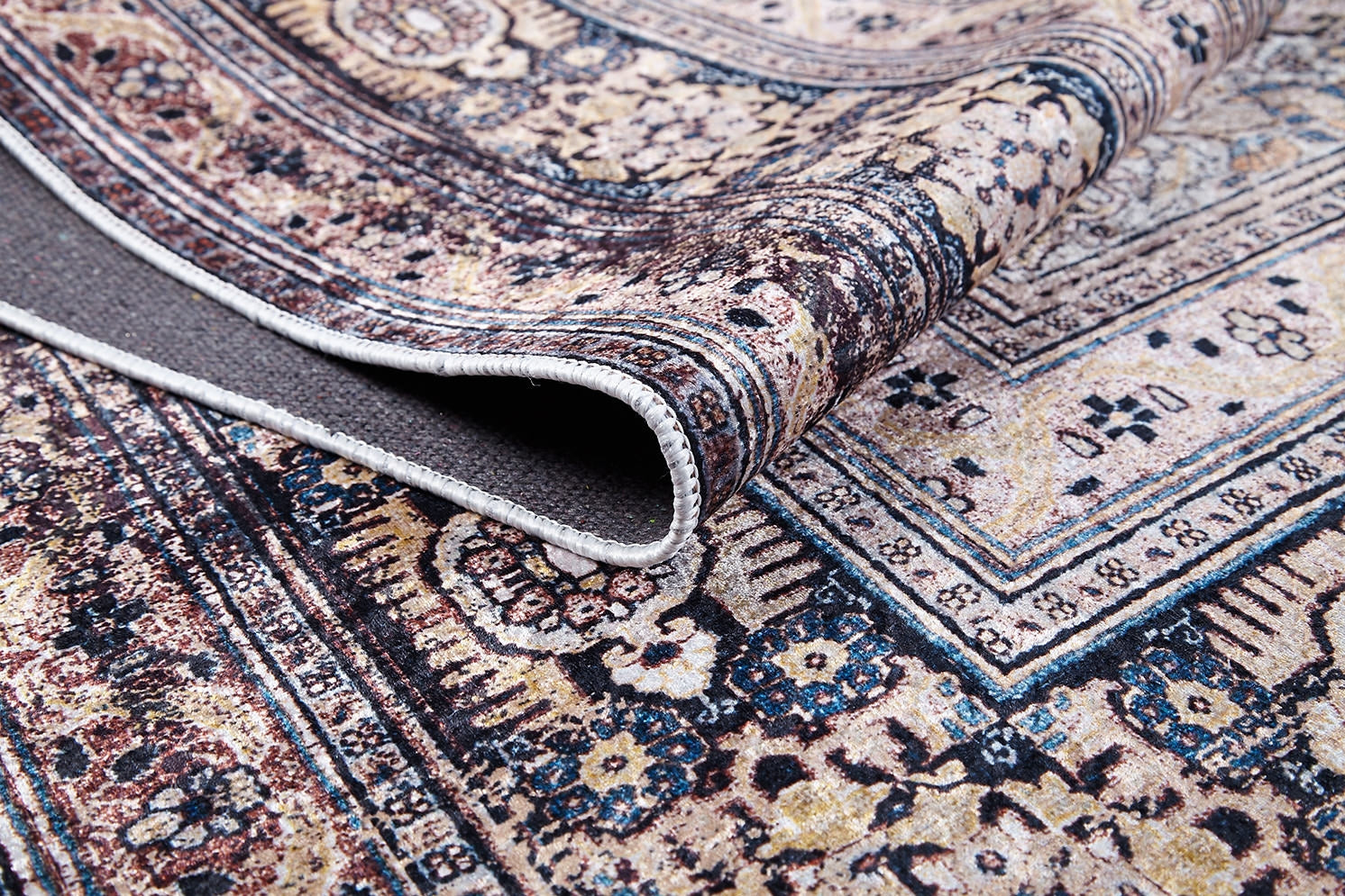 A close-up of the Vintage Charm - Washable Rug - JR1933 (Custom Size) displays its intricate floral and geometric beige, blue, and brown patterns with a folded corner revealing textured backing—perfect for allergy-sensitive or high-traffic spaces.