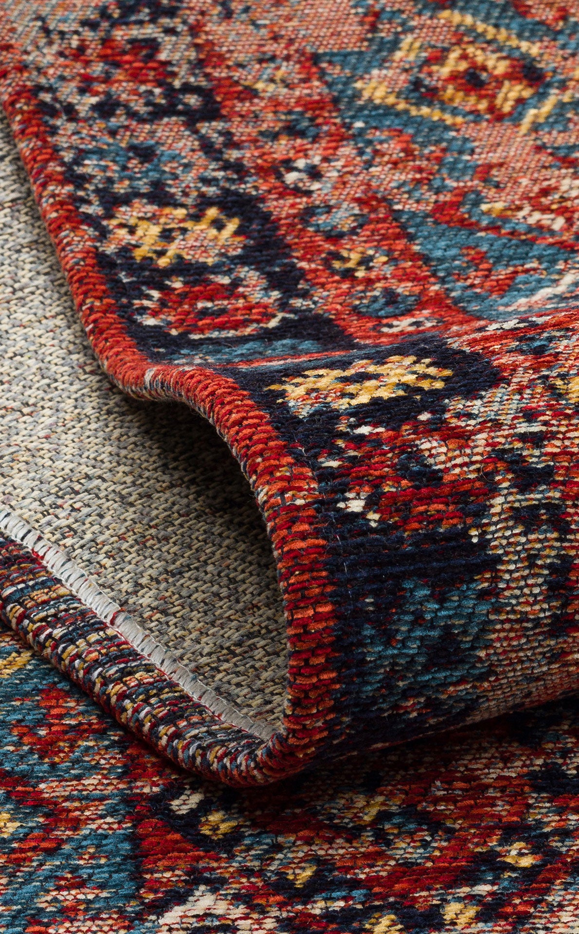 A close-up of the Vintage Echo - Washable Kilims - AND04 shows a rolled-up rug with vibrant red, blue, yellow, and cream hues in intricate geometric and floral patterns bordered by detailed designs.