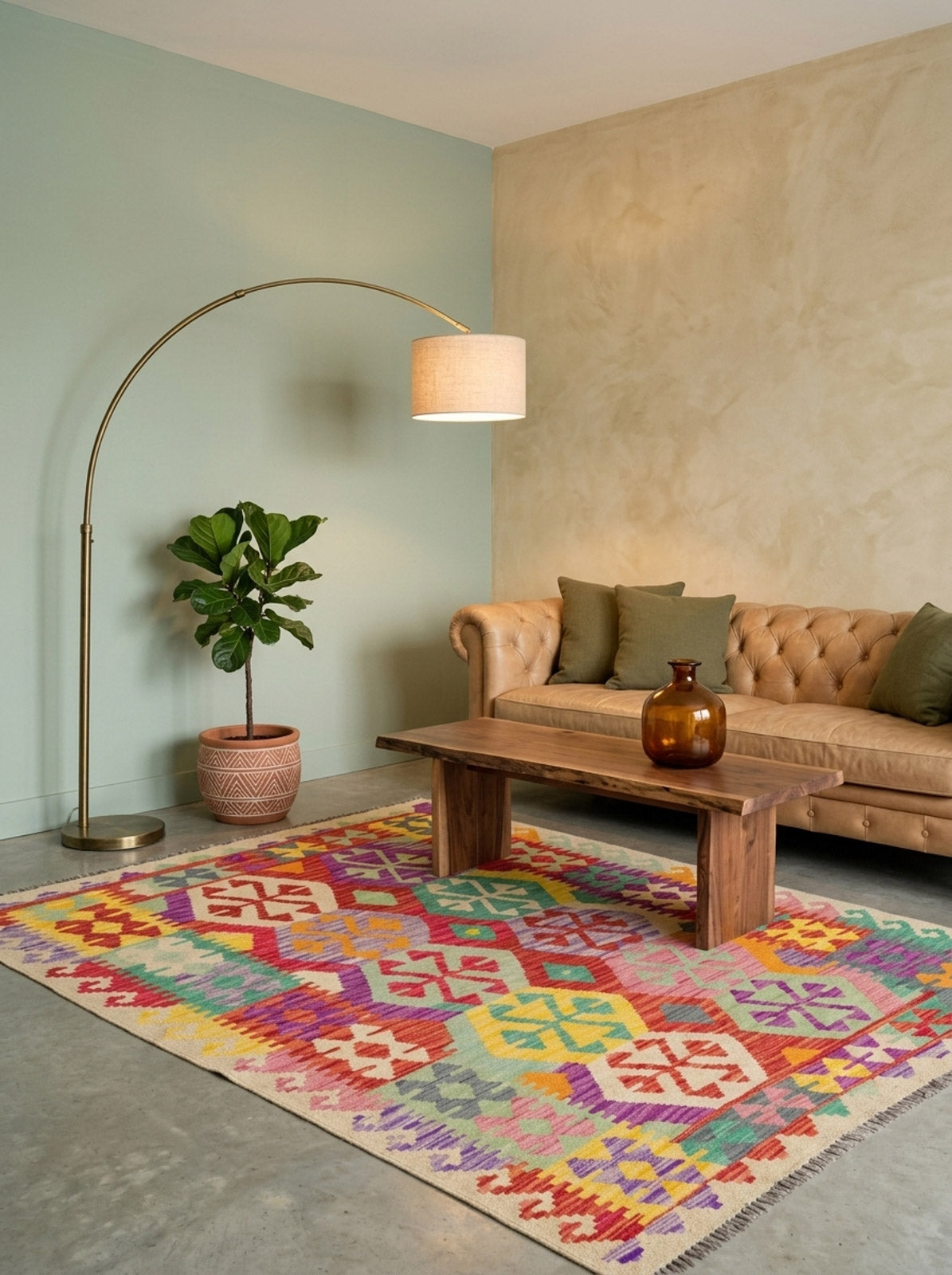 A cozy living room featuring a tan tufted sofa, green cushions, a wooden coffee table, the Vintage Heritage - Handwoven Kilim rug, a fiddle-leaf fig plant, brown glass vase, and an arched floor lamp against pastel walls.
