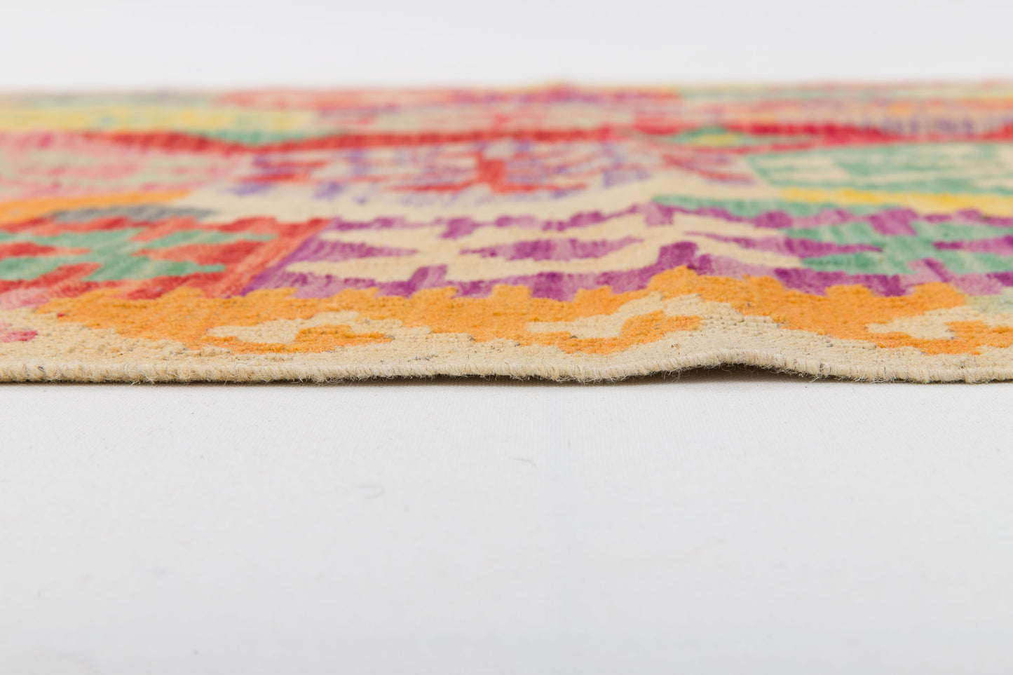 Close-up side view of the Vintage Heritage - Handwoven Kilim, showcasing its vibrant geometric patterns in orange, green, red, and purple. The flatweave wool texture and thickness are clearly visible against a white surface.