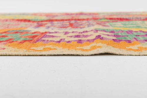Load image 1 in gallery view. Close-up side view of the Vintage Heritage - Handwoven Kilim, showcasing its vibrant geometric patterns in orange, green, red, and purple. The flatweave wool texture and thickness are clearly visible against a white surface.