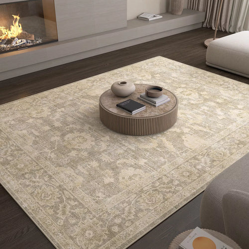 Load image 1 in gallery view. A living room featuring the Vintage Linen - Washable Rug - JRN1028, perfect for allergy-sensitive and high-traffic areas, with a round coffee table holding two vases and books, dark wood flooring, fireplace, and neutral-toned furniture.