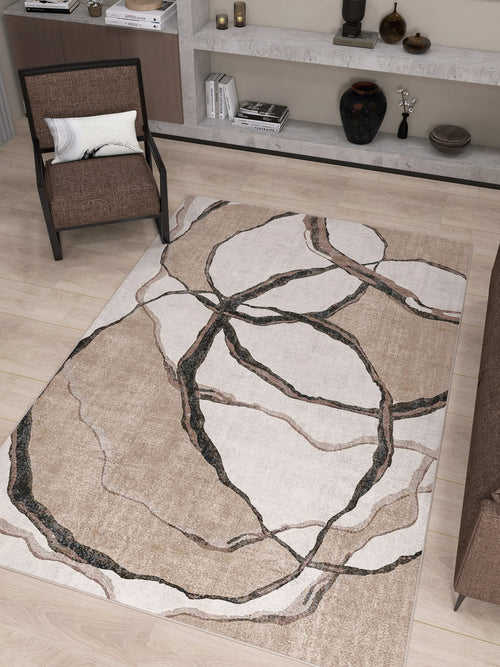 Load image 1 in gallery view. A modern living room with the Vintage Muse - Washable Rug - JRN47, a beige flat weave rug with an abstract pattern, a brown armchair with cushion, brown sofa edge, light wood floors, and shelves displaying vases and books.