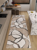 A modern kitchen with light wood floors, a marble island, beige cabinets, and the Vintage Muse - Washable Rug - JRN47 in an abstract branch pattern. A wooden table with fruit and flowers stands near two wooden stools.