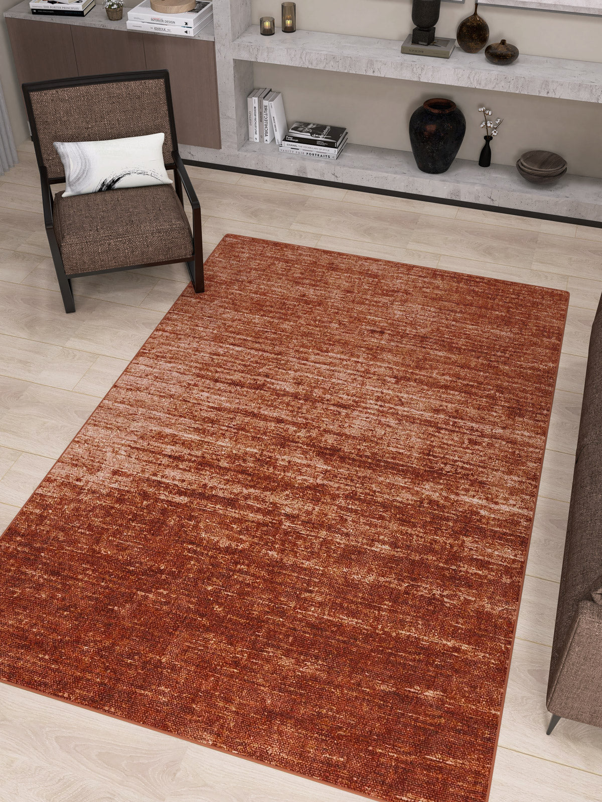 A modern living room featuring the Vintage Reverie - Washable Rug - JRN31 in deep red ombre design on light wood floors, placed near a brown chair with a white pillow and built-in shelves showcasing decor, books, and vases.