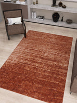 A modern living room featuring the Vintage Reverie - Washable Rug - JRN31 in deep red ombre design on light wood floors, placed near a brown chair with a white pillow and built-in shelves showcasing decor, books, and vases.
