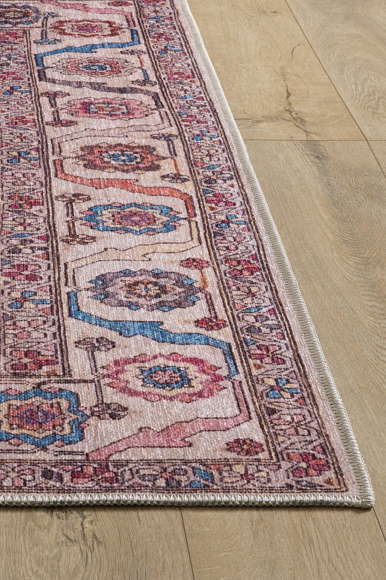 A close-up of the Vivencia Authentic Washable Rug - LCC3016 (Outlet) US in pink, blue, and cream with geometric and floral designs on a light wooden floor, showing the detailed border of this durable, washable rug.