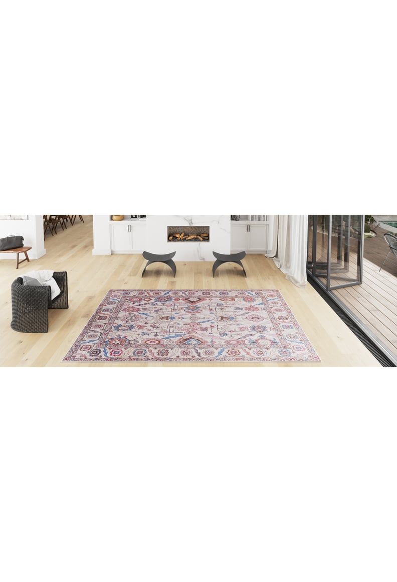 A bright, modern living room with light wood floors, a Vivencia Authentic Washable Rug - LCC3016 (Custom Size) in colorful patterns, a wicker chair with a white blanket, two black stools, and glass doors—ideal for allergy-sensitive homes.