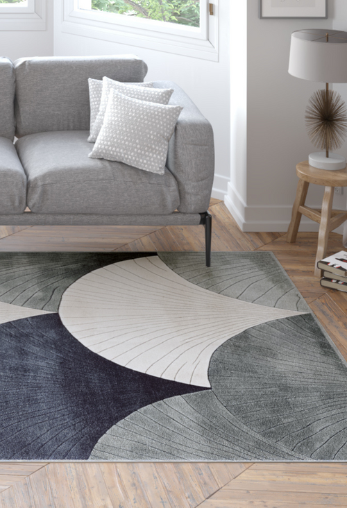 Load image 1 in gallery view. A modern living room with a gray sofa, patterned white pillows, a wooden side table and lamp, and the Vivian Modern Washable Area Rug - MDJ010 (Custom Size) in black, gray, and cream abstract shapes on a wooden floor.