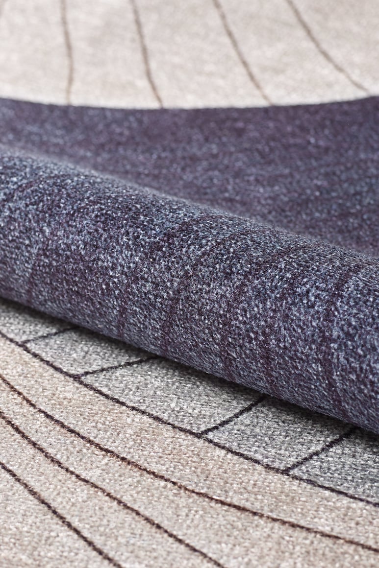 A close-up of the Vivian Modern Washable Area Rug - MDJ010 (Custom Size), rolled up to show its gray-anthracite base and geometric pattern in beige, gray, and dark purple with curved and straight lines for a modern, textured look.