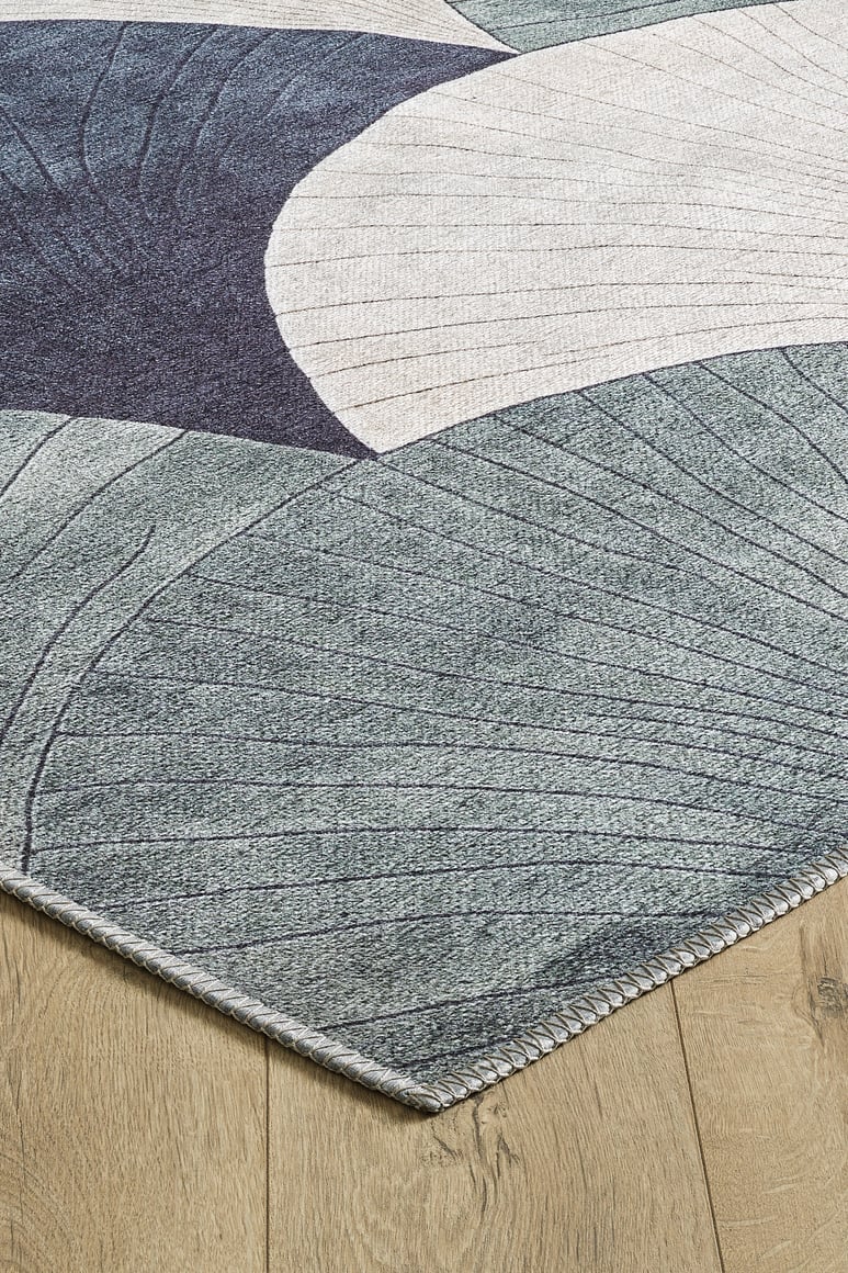 A close-up of the Vivian Modern Washable Area Rug - MDJ010 (Custom Size), featuring curved geometric shapes in blue, gray, and beige on a light wood floor. The high-traffic rug has a stitched border for added durability.