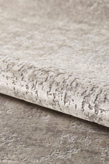 Close-up of the Vortexia Light Premium Rug - M472D in beige and light gray. This machine-made rug features a subtle abstract pattern, a soft, slightly raised surface, and is partially rolled at the edge for added style.