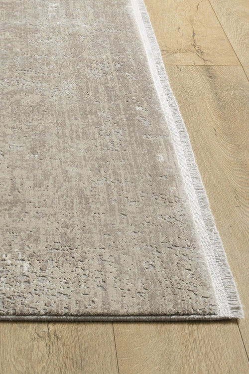 Load image 1 in gallery view. A close-up of the Vortexia Light Premium Rug - M472D showcases its textured neutral beige pattern and short fringes, beautifully placed on light wood flooring.