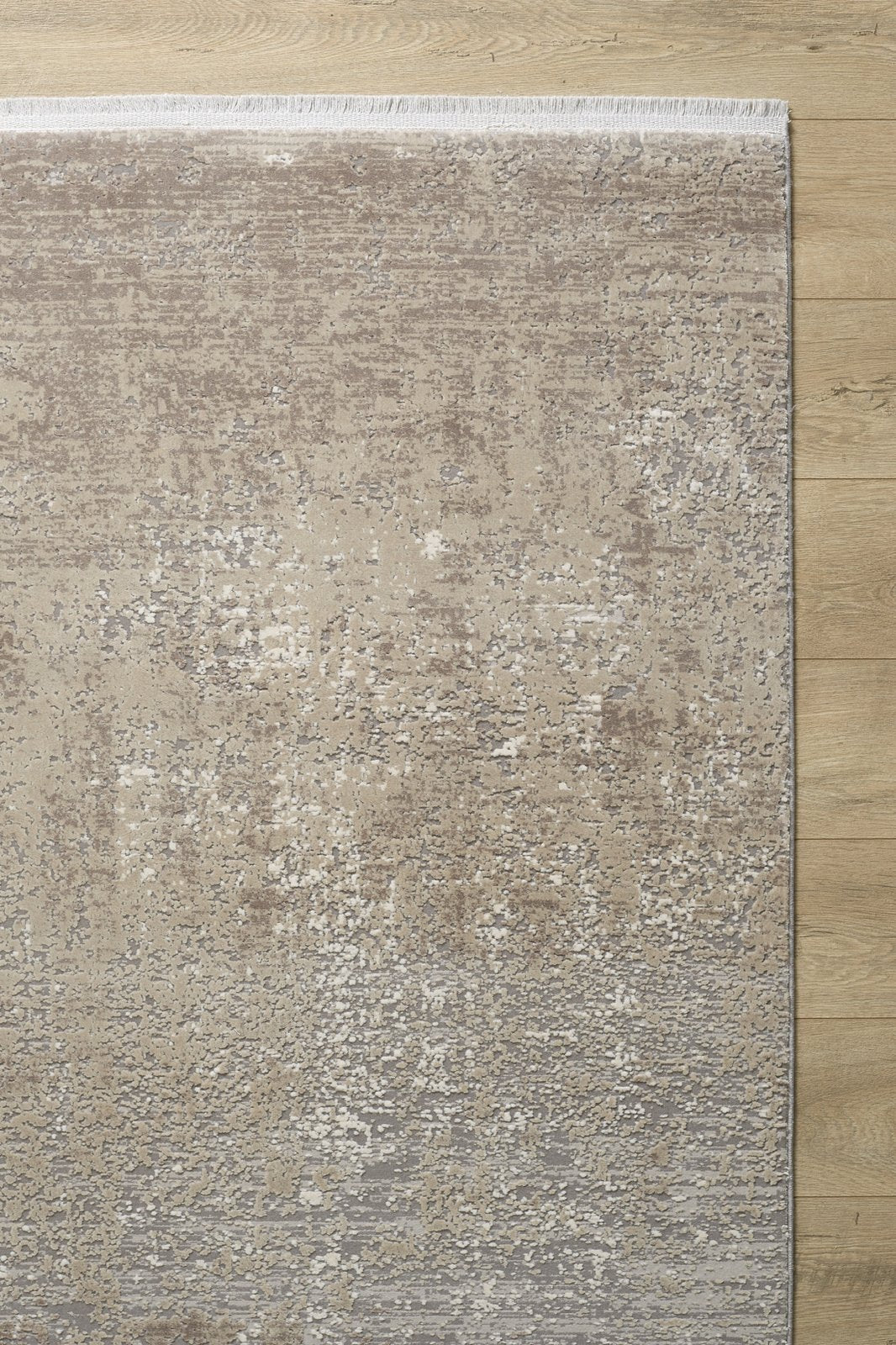 The Vortexia Light Premium Rug - M472D is a rectangular contemporary rug with a textured abstract pattern in neutral beige and taupe, featuring a subtle gradient, short fringe on one edge, and placed on a light wood floor.