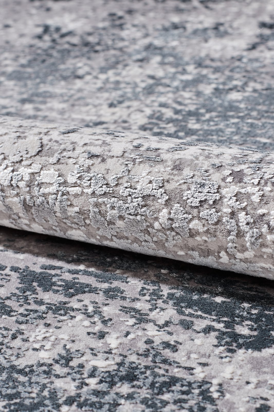 A close-up of the Vortexia Silver Premium Rug - M472A, showcasing its textured surface in gray, white, and dark blue with an abstract mottled design and subtle distressed details.